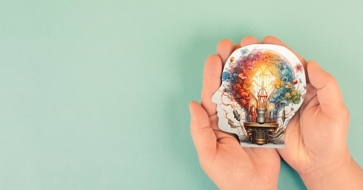 Hands holding an illustrated head with a colourful imagination lightbulb representing creativity in schools