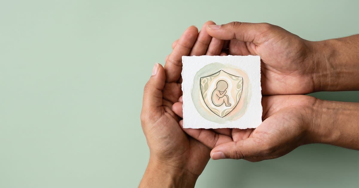 Two pairs of hands gently cradling a small watercolour shield with a child silhouette inside, set against a soft sage background. A symbol of protective, pain-free care.